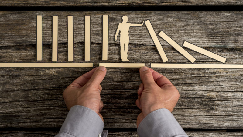 hands putting together wood statues of businessman holding dominos up